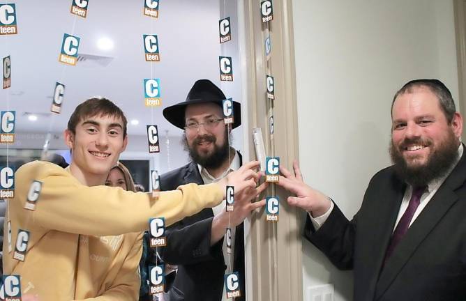 CTeen leader Ariel Koyfman of Chester recites the blessing and affixes the Mezuzah scroll to the doorpost of the new CTeen Lounge at Chabad of Orange County, guided by Rabbi Shimon Rivkin, director of CTeen International, and Rabbi Pesach Burston, director, Chabad of Orange County.