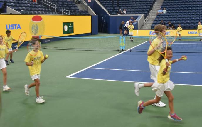 Twenty-four players from Matchpoint Tennis in Goshen take a lap around the court on Louis Armstong Stadium before breaking into pairs and rallying.